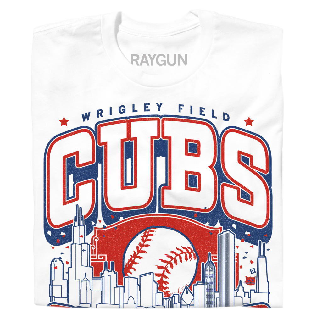 A folded white t-shirt with red and blue print. The center depicts Chicago's skyline with a large baseball peaking out from behind it. Text from top to bottom reads "Wrigley Field. Cubs. Chicago. Since 1870. Fly The W."