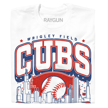 A folded white t-shirt with red and blue print. The center depicts Chicago's skyline with a large baseball peaking out from behind it. Text from top to bottom reads "Wrigley Field. Cubs. Chicago. Since 1870. Fly The W."