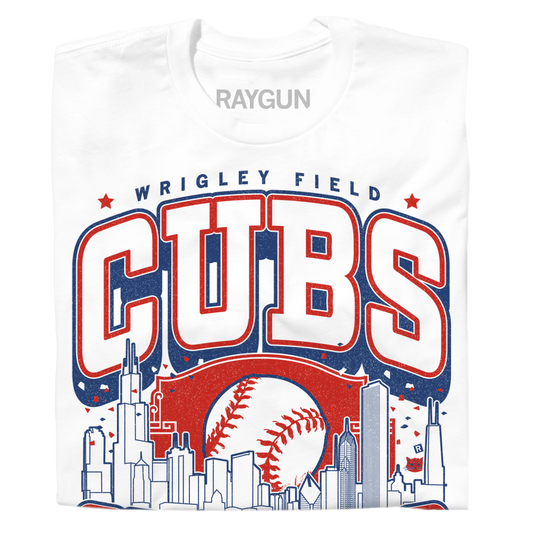 A folded white t-shirt with red and blue print. The center depicts Chicago's skyline with a large baseball peaking out from behind it. Text from top to bottom reads "Wrigley Field. Cubs. Chicago. Since 1870. Fly The W."