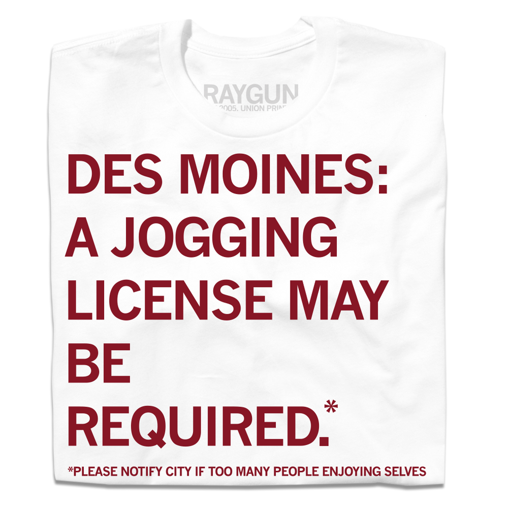 A folded white t-shirt with cardinal ink that reads "Des Mines: a jogging license may be required.* *Please notify city if too many people enjoying themselves."