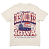 Cream-colored Des Moines t-shirt featuring an illustration of the Iowa state capital, an umbrella, and text reading Des Moines, Iowa, French for The Moines, and The Travelers with the slogan Let us exceed your already low expectations.
