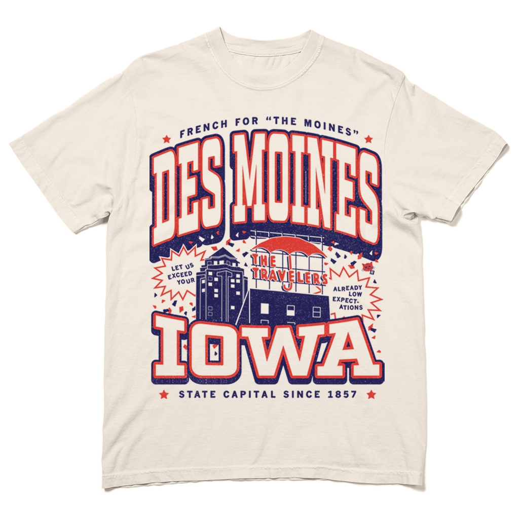 Cream-colored Des Moines t-shirt featuring an illustration of the Iowa state capital, an umbrella, and text reading Des Moines, Iowa, French for The Moines, and The Travelers with the slogan Let us exceed your already low expectations.