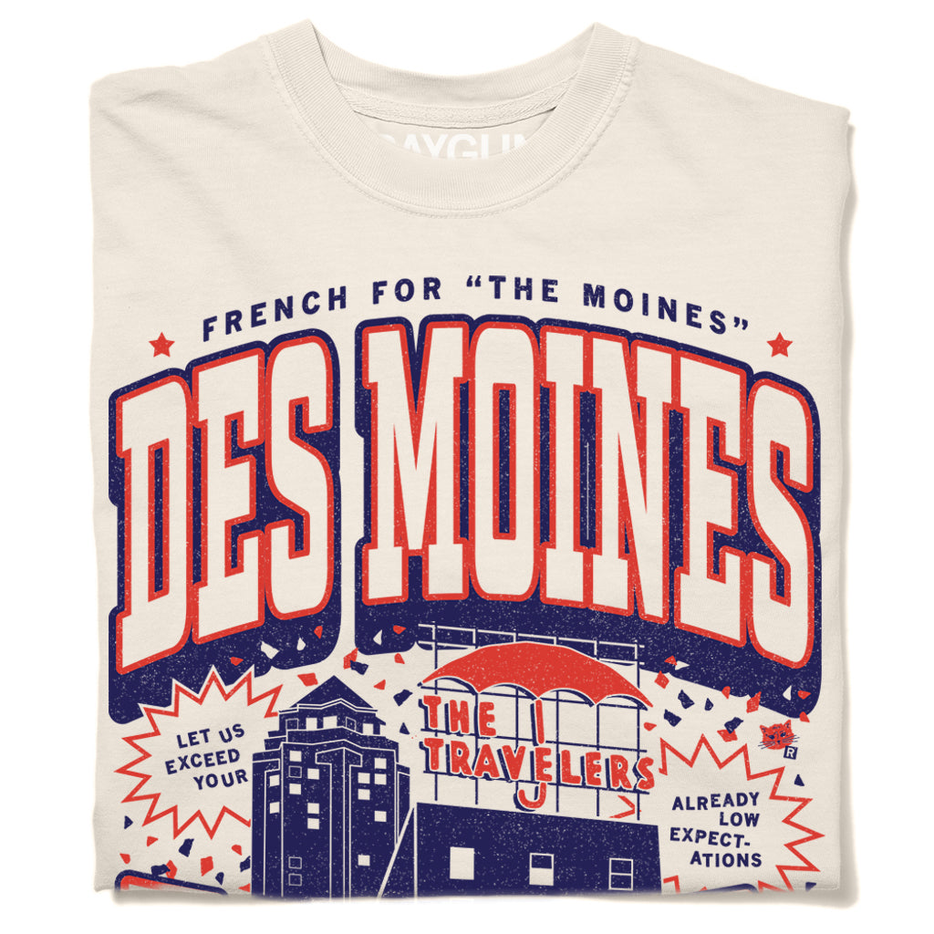 Off-white heavyweight cotton t-shirt with a graphic that reads The Moines Des Moines, featuring an illustration of the Travelers Insurance building and the text Let us exceed your already low expectations on this Des Moines t-shirt.