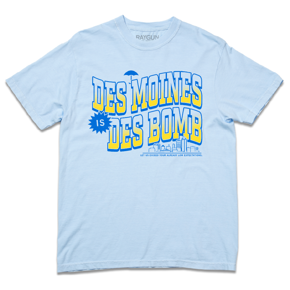 Comfort Colors heavyweight light blue t-shirt with bright gold and blue ink text that reads "Des Moines is Des Bomb. Let us exceed your already low expectations" with a small Des Moines skyline in the bottom right.