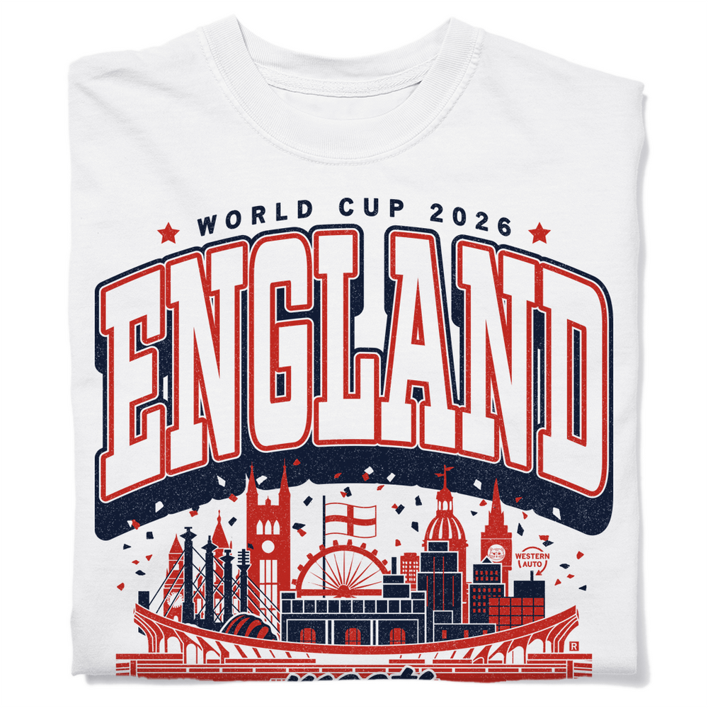 A folded white heavyweight t-shirt with navy and red ink. Text from top to bottom reads "World Cup 2026: England meets Kansas City. Bangers &amp; mash meets bbq." In the center is an illustration mixing notable building from England and Kansas City together.