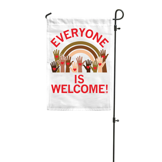 A RAYGUN garden flag reading EVERYONE IS WELCOME! above an illustration of diverse hands raised in front of a rainbow.