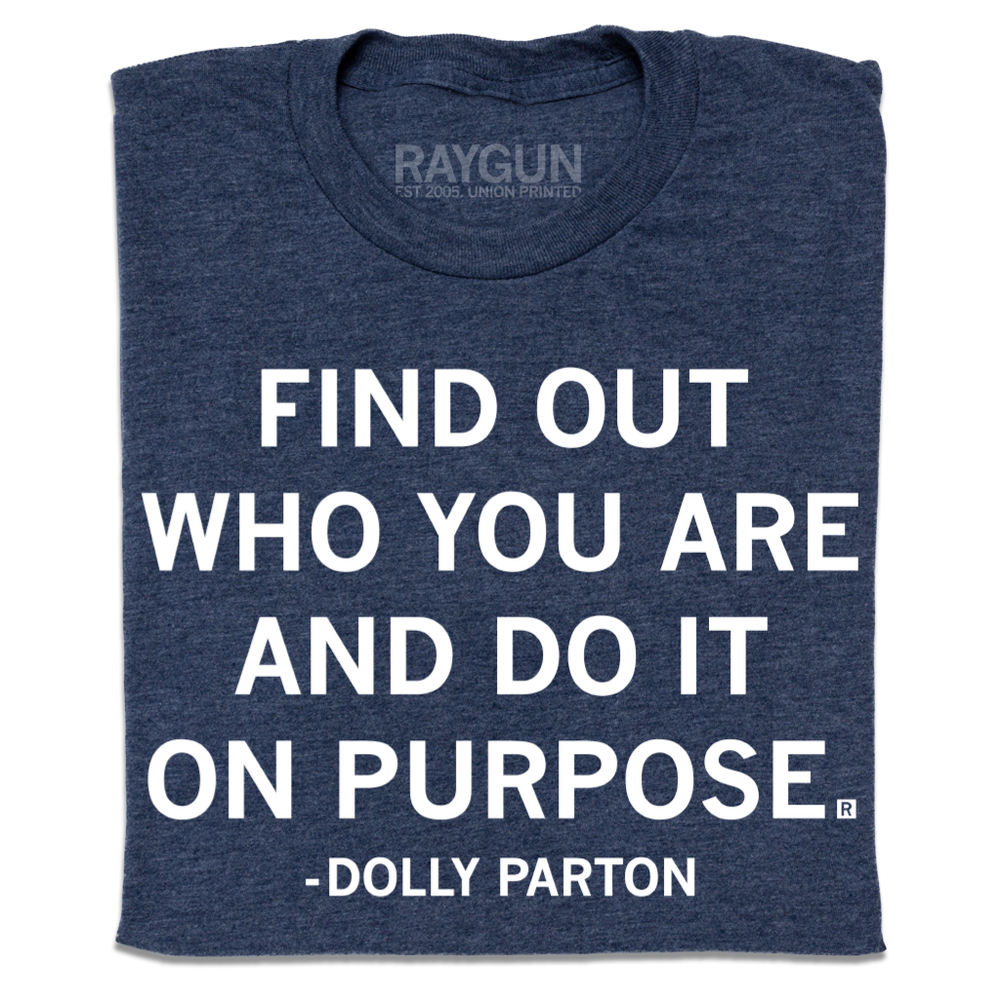 A folded heather navy t-shirt with centered white print text that says, ""Find out who you are and do it on purpose." - Dolly Parton"