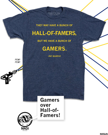 An image of a RAYGUN shirt that says "They May have a bunch of Hall-of-Famers, but we have a bunch of Gamers." Pat Murphy. The shirt is golden ink on a navy shirt. A RAYGUN logo is in the background. A cartoon Badger named Madi is saying "Gamers over Hall-of-Famers." 