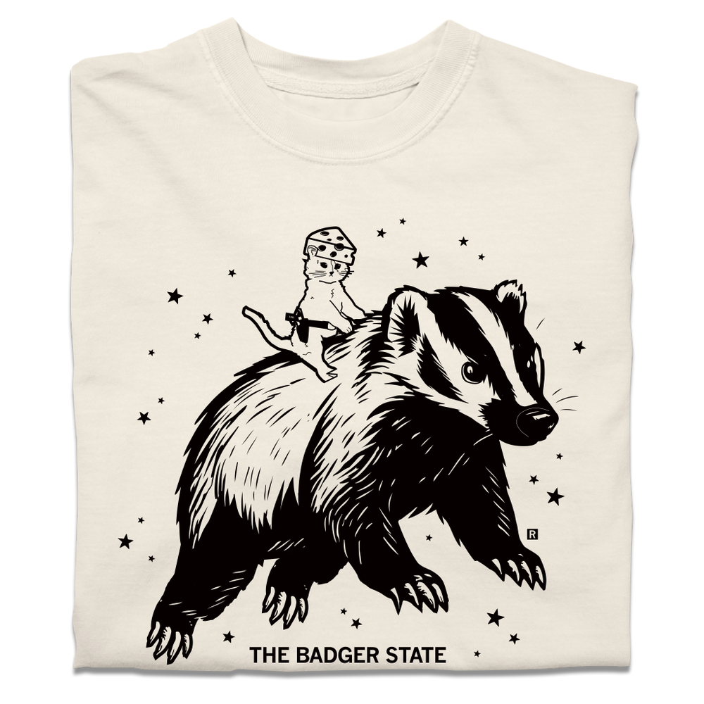 A folded ivory heavyweight t-shirt with a black ink graphic of a cat wearing a cheese hat riding a giant badger above the text "The Badger State"