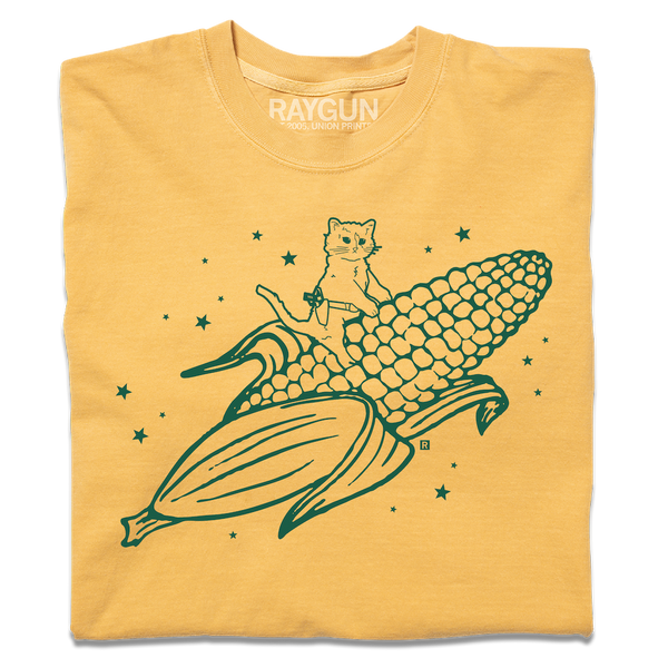 A folded heavyweight yellow t-shirt with kelly green ink print depicting RAYGUN's cat mascot riding a giant ear of corn.