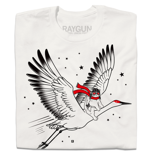 A folded dull white t-shirt with black and bright red ink depicting RAYGUN's cat mascot riding a giant crane through the sky while wearing a pilot helmet and a scarf.
