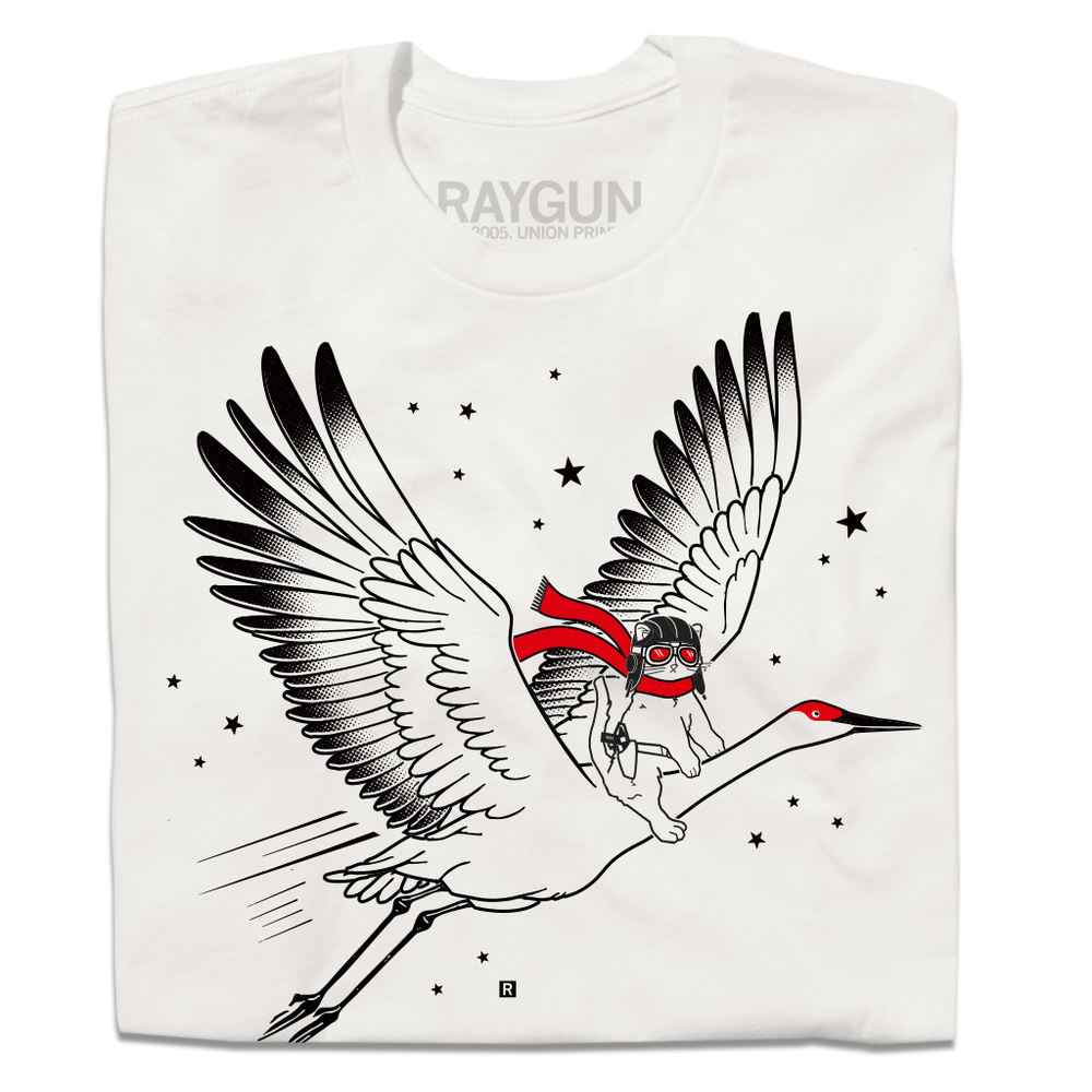 A folded dull white t-shirt with black and bright red ink depicting RAYGUN's cat mascot riding a giant crane through the sky while wearing a pilot helmet and a scarf.