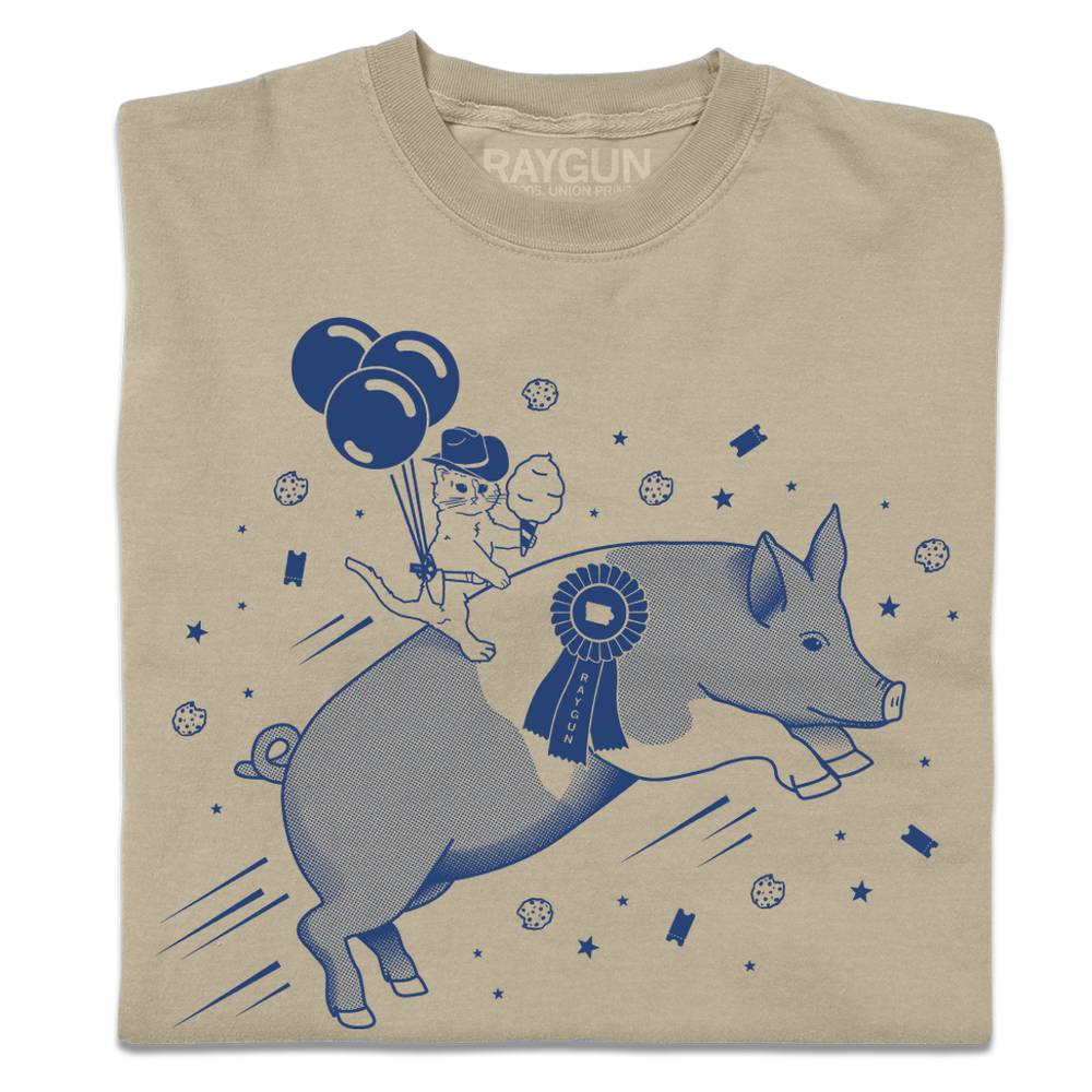 A folded khaki heavyweight t-shirt with royal blue print depicting a hat with a cowboy hat holding cotton candy while riding a giant pig.