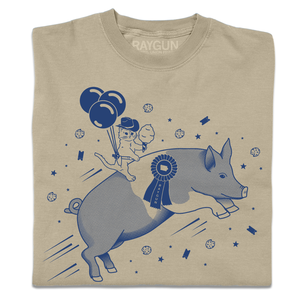 A folded khaki heavyweight t-shirt with royal blue print depicting a hat with a cowboy hat holding cotton candy while riding a giant pig.