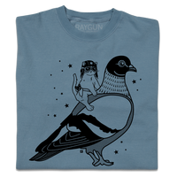A folded denim blue heavyweight t-shirt with black ink print illustrating RAYGUN's cat mascot riding a giant pigeon.