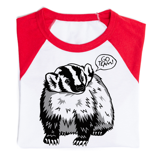 White and red baseball-style t-shirt featuring a black and white illustration of a badger with a speech bubble that says, GO TEAM!. Designed and printed in the USA.