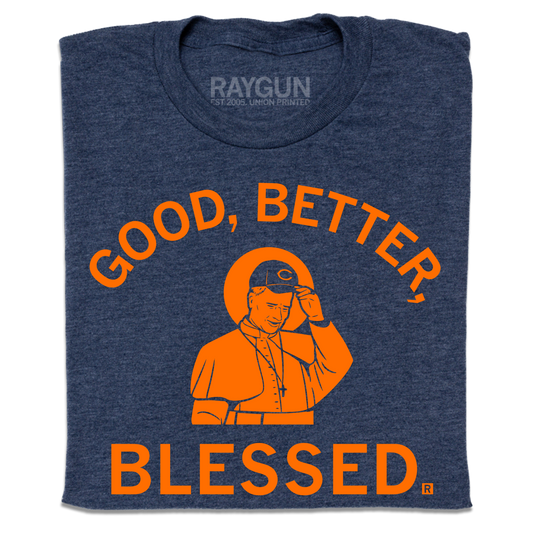 A folded heather navy t-shirt with orange print. Curved text at the top says, "Good, Better," and straight text below adds "Blessed." In the center is an illustration of Pope wearing a football team hat.