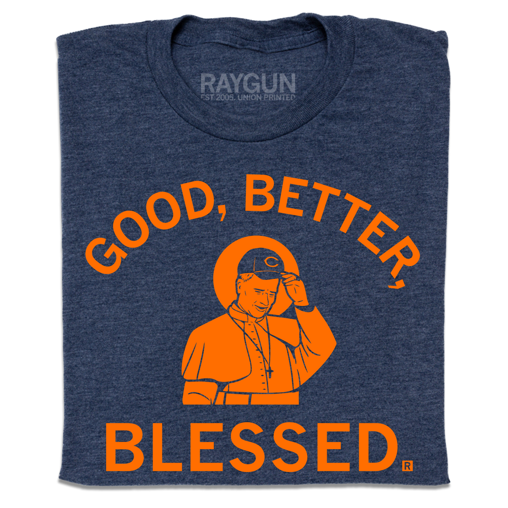 A folded heather navy t-shirt with orange print. Curved text at the top says, "Good, Better," and straight text below adds "Blessed." In the center is an illustration of Pope wearing a football team hat.