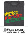 A charcoal gray Good Trouble T-shirt with the text Good Trouble Lives On printed in yellow, red, and green paint-stroke style blocks.