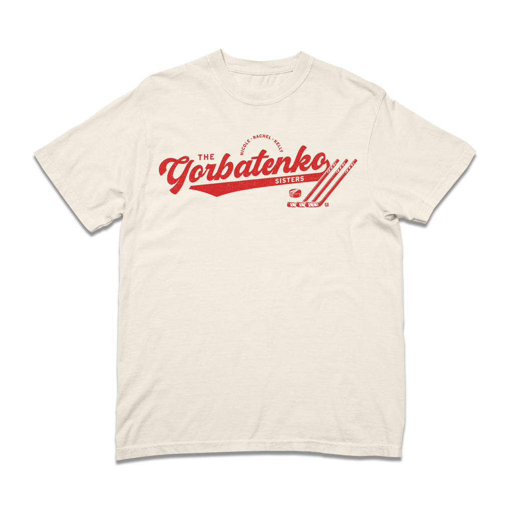 Red script text on an ivory comfort colors shirt that says, "The Gorbatenko Sissters. Nicole, Rachel, Kelly" with three hockey sticks and a puck laid flat.