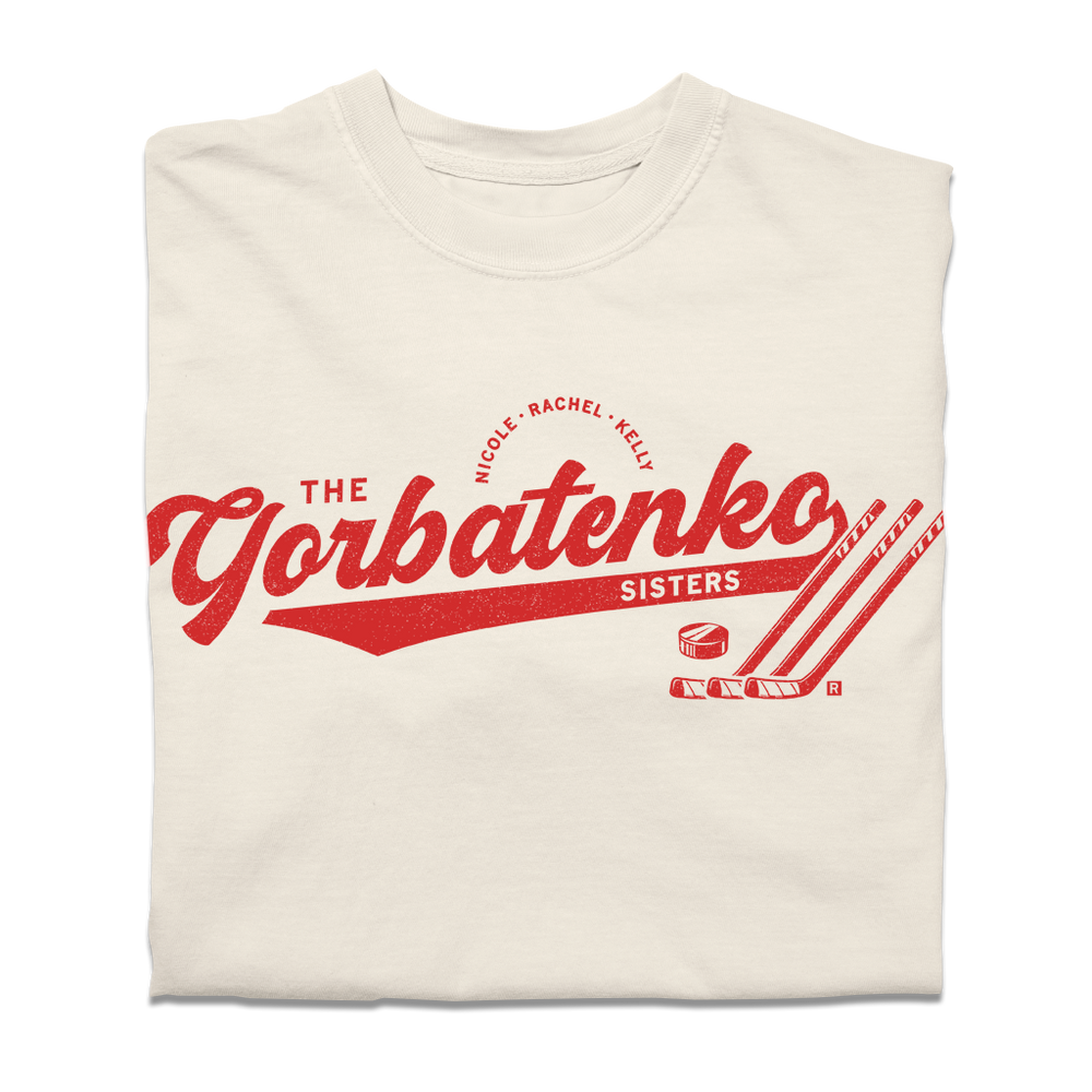 Red script text on an ivory comfort colors shirt that says, "The Gorbatenko Sissters. Nicole, Rachel, Kelly" with three hockey sticks and a puck.
