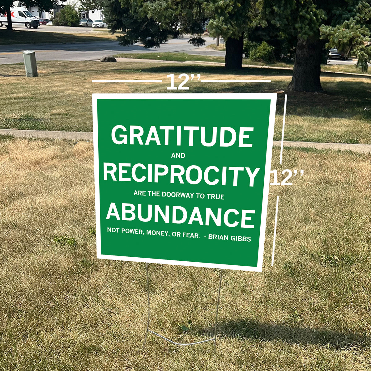 A 12x12-inch green gratitude yard sign with white text reading, Gratitude and reciprocity are the doorway to true abundance. Not power, money, or fear. - Brian Gibbs, featuring overlaid measurement lines.