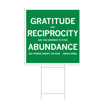 A green RAYGUN yard sign with white text that reads: GRATITUDE AND RECIPROCITY ARE THE DOORWAY TO TRUE ABUNDANCE. NOT POWER, MONEY, OR FEAR. - BRIAN GIBBS.