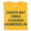 Folded heather yellow shirt with centered, dark green text that says, "GREEN BAY OWNS CHICAOG HAMMOND, IN" with a line through "CHICAGO."