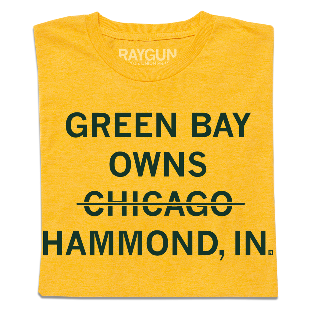 Folded heather yellow shirt with centered, dark green text that says, "GREEN BAY OWNS CHICAOG HAMMOND, IN" with a line through "CHICAGO."