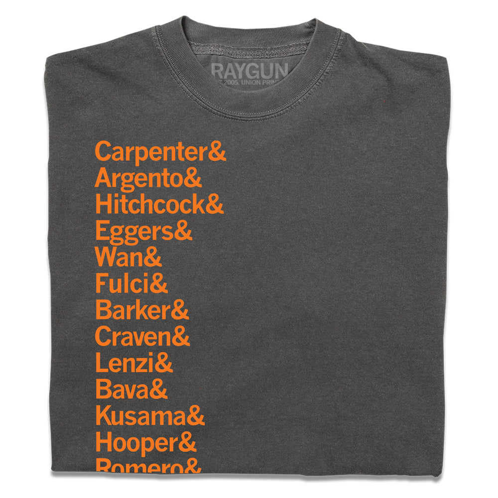 A folded heavyweight dark grey t-shirt with left-aligned orange ink that says, "Carpenter &amp; Argento &amp; Hitchcock &amp; Eggers &amp; Wan &amp; Fulci &amp; Barker &amp; Craven &amp; Lenzi &amp; Bava &amp; Kusama &amp; Hooper &amp; Romero &amp; Peele &amp; Castle &amp; Cronenberg &amp; del Toro." in a long list.