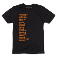 A short-sleeve black t-shirt with left-aligned orange ink in a long list that reads "Carpenter &amp; Argento &amp; Hitchcock &amp; Eggers &amp; Wan &amp; Fulci &amp; Barker &amp; Craven &amp; Lenzi &amp; Bava &amp; Kusama &amp; Hooper &amp; Romero &amp; Peele &amp; Castle &amp; Cronenberg &amp; del Toro."