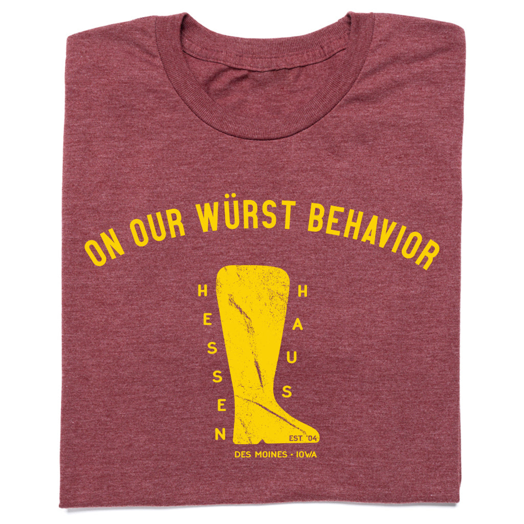 Heather burgundy t-shirt featuring the text ON OUR WÜRST BEHAVIOR in yellow above a graphic of a boot containing the words HESSEN HAUS, EST 04, and DES MOINES - IOWA.