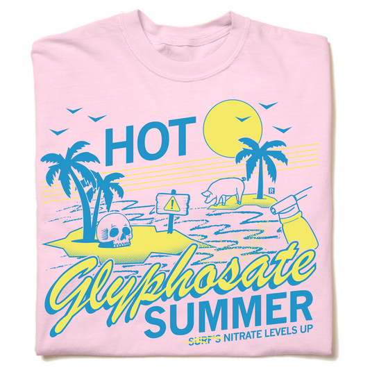 A light pink, garment-dyed heavyweight t-shirt featuring a beach scene with a skull, a pig, a warning sign, and a spray bottle, accompanied by the text: HOT Glyphosate SUMMER SURFS NITRATE LEVELS UP.
