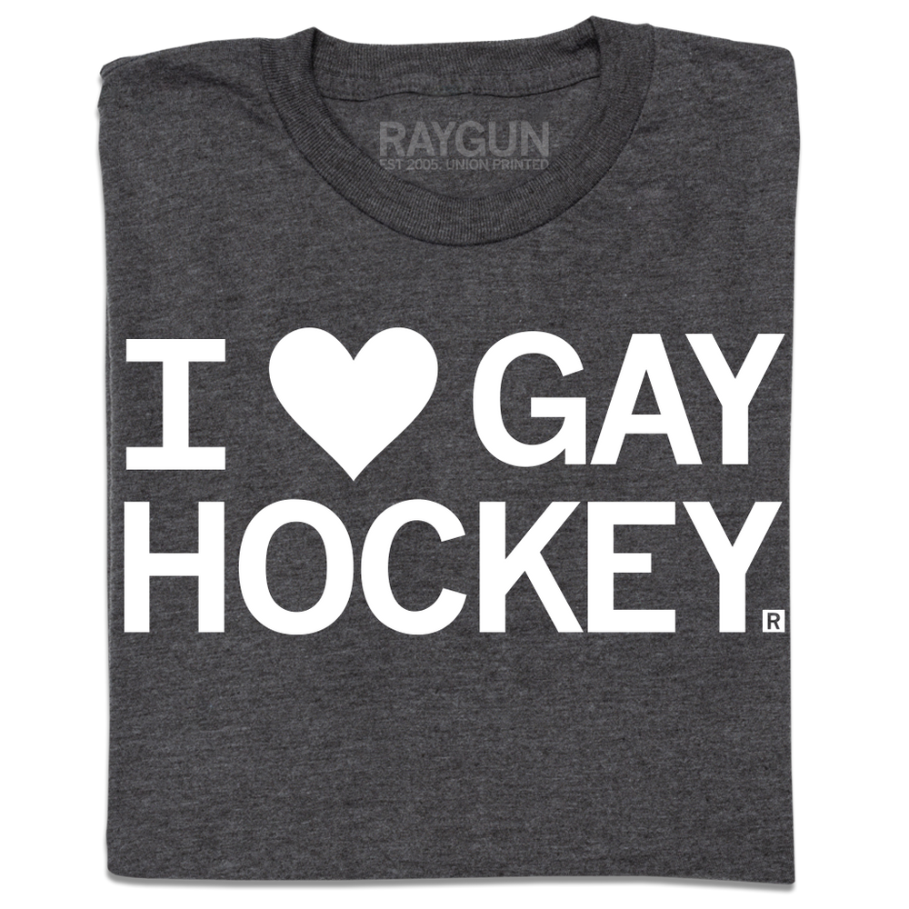 A folded charcoal t-shirt with white ink text that reads, "I heart gay hockey" where the heard is an emoji rather than spelled out.