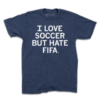 A heather denim t-shirt with centered white text that reads "I love soccer, but I hate FIFA."