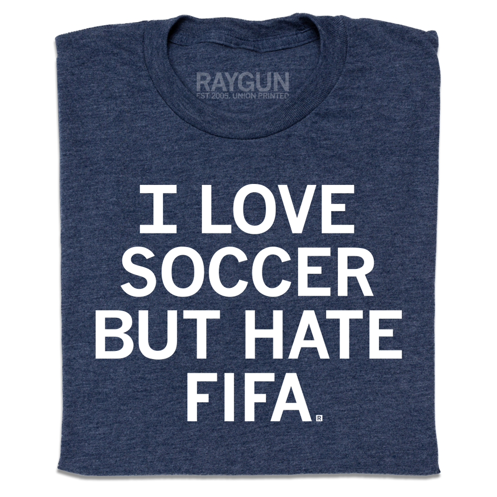A folded heather navy t-shirt with centered white text that reads "I love soccer, but I hate FIFA."