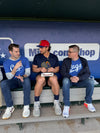 Three men sit on a RAYGUN dugout bench, with the man in the center holding a small box.