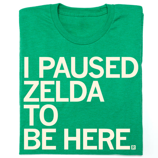 A heather green t-shirt with left aligned cream ink text that says, "I Paused Zelda to be Here" in all caps.