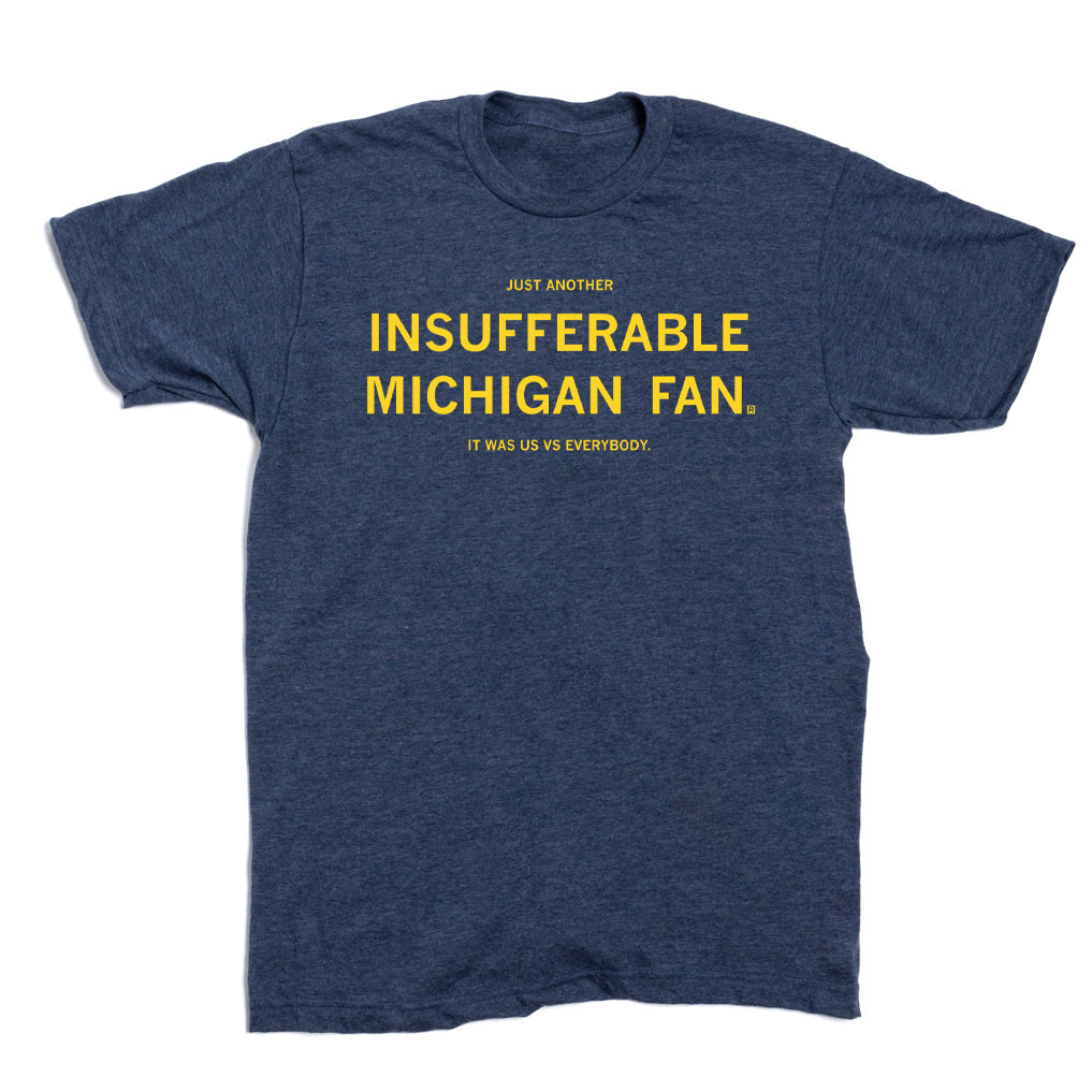 A navy blue RAYGUN t-shirt with yellow text that reads JUST ANOTHER INSUFFERABLE MICHIGAN FAN. IT WAS US VS EVERYBODY.