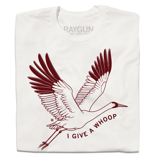 A folded off white t-shirt with maroon ink depicting a Whooping Crane in flight with the text "I Give a Whoop" underneath it.
