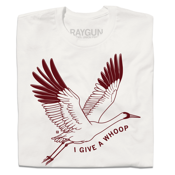 A folded off white t-shirt with maroon ink depicting a Whooping Crane in flight with the text 