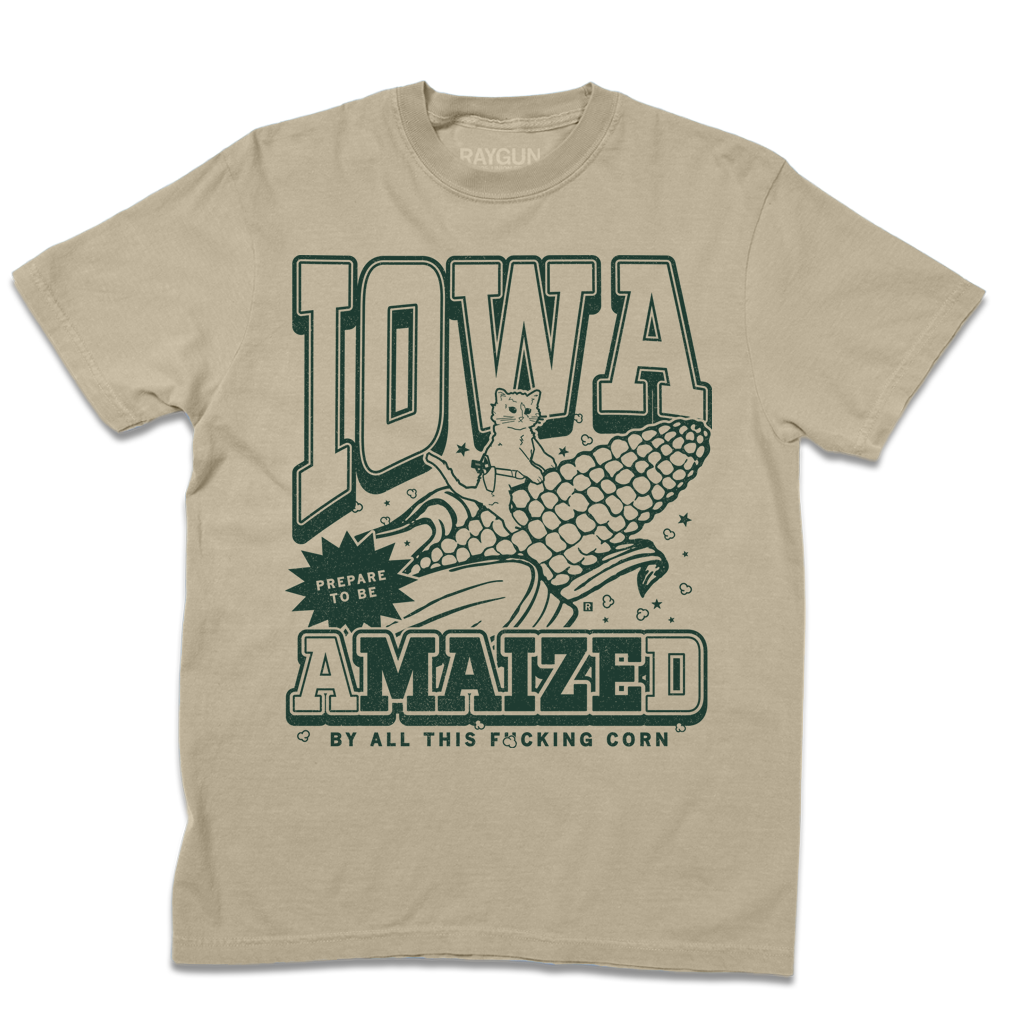 Tan garment-dyed t-shirt featuring a cat sitting on a large ear of corn with dark green text reading IOWA, PREPARE TO BE AMAIZED, and BY ALL THIS F*CKING CORN.