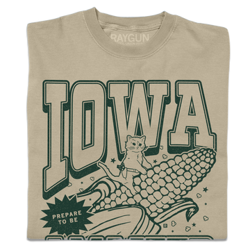 Tan garment-dyed t-shirt featuring a dark green graphic of a cat riding a giant ear of Iowa corn with the text IOWA and PREPARE TO BE.
