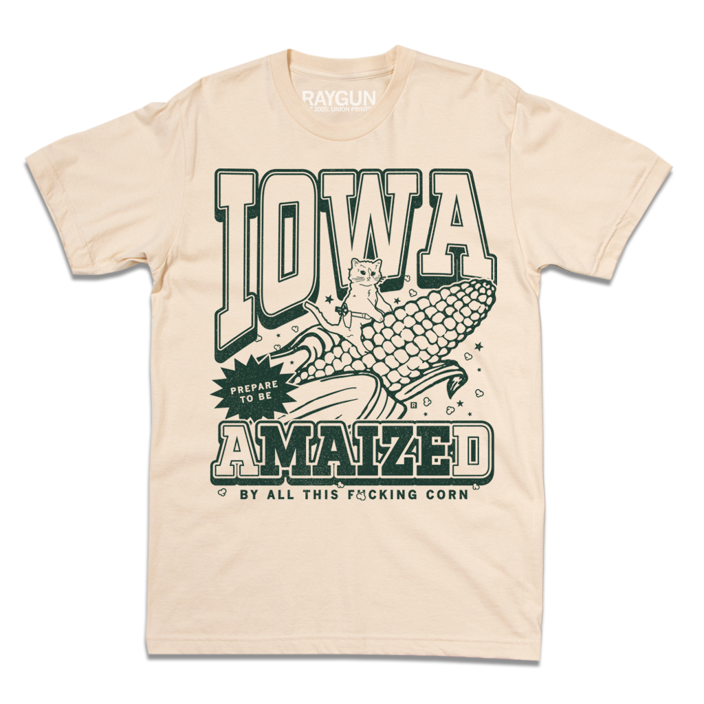 Cream t-shirt with dark green ink that says, "Iowa: Prepare to be aMAIZEd by all this f*cking corn" along with an illustration of a cat riding a giant ear of corn.