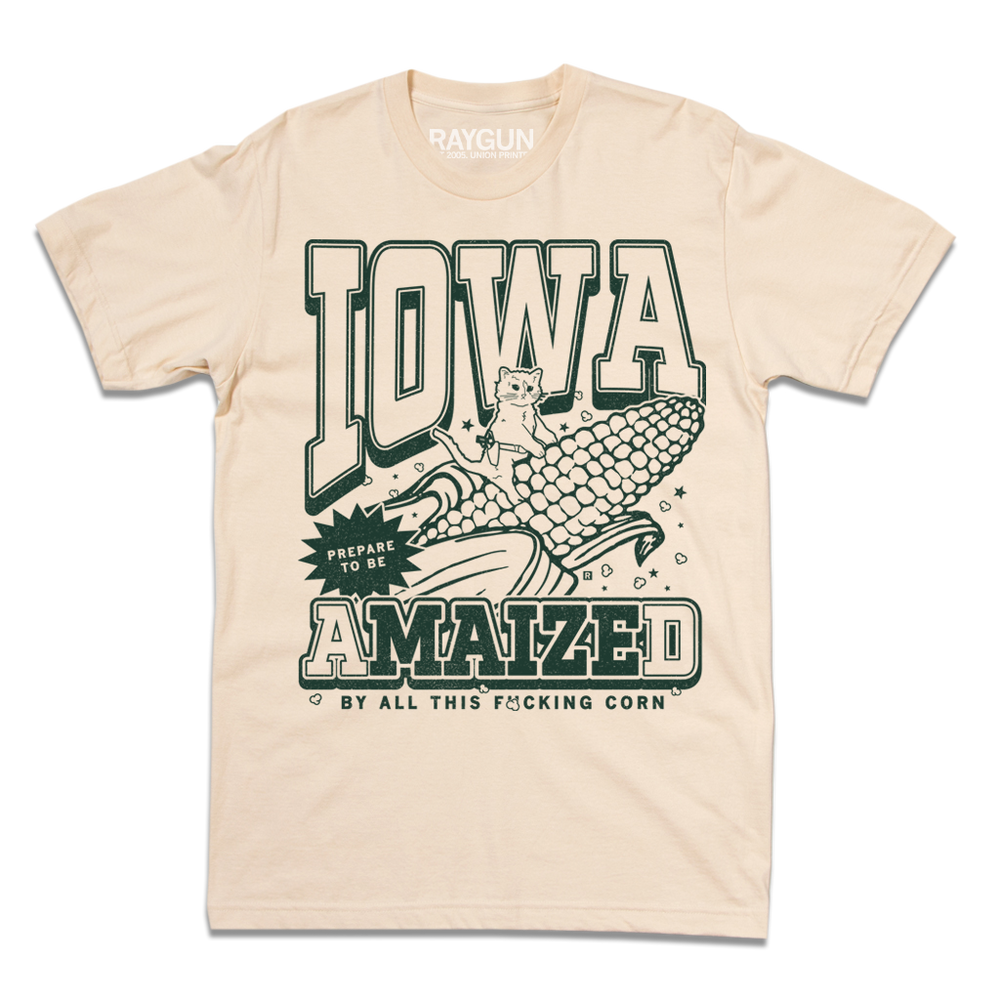 Cream t-shirt with dark green ink that says, "Iowa: Prepare to be aMAIZEd by all this f*cking corn" along with an illustration of a cat riding a giant ear of corn.