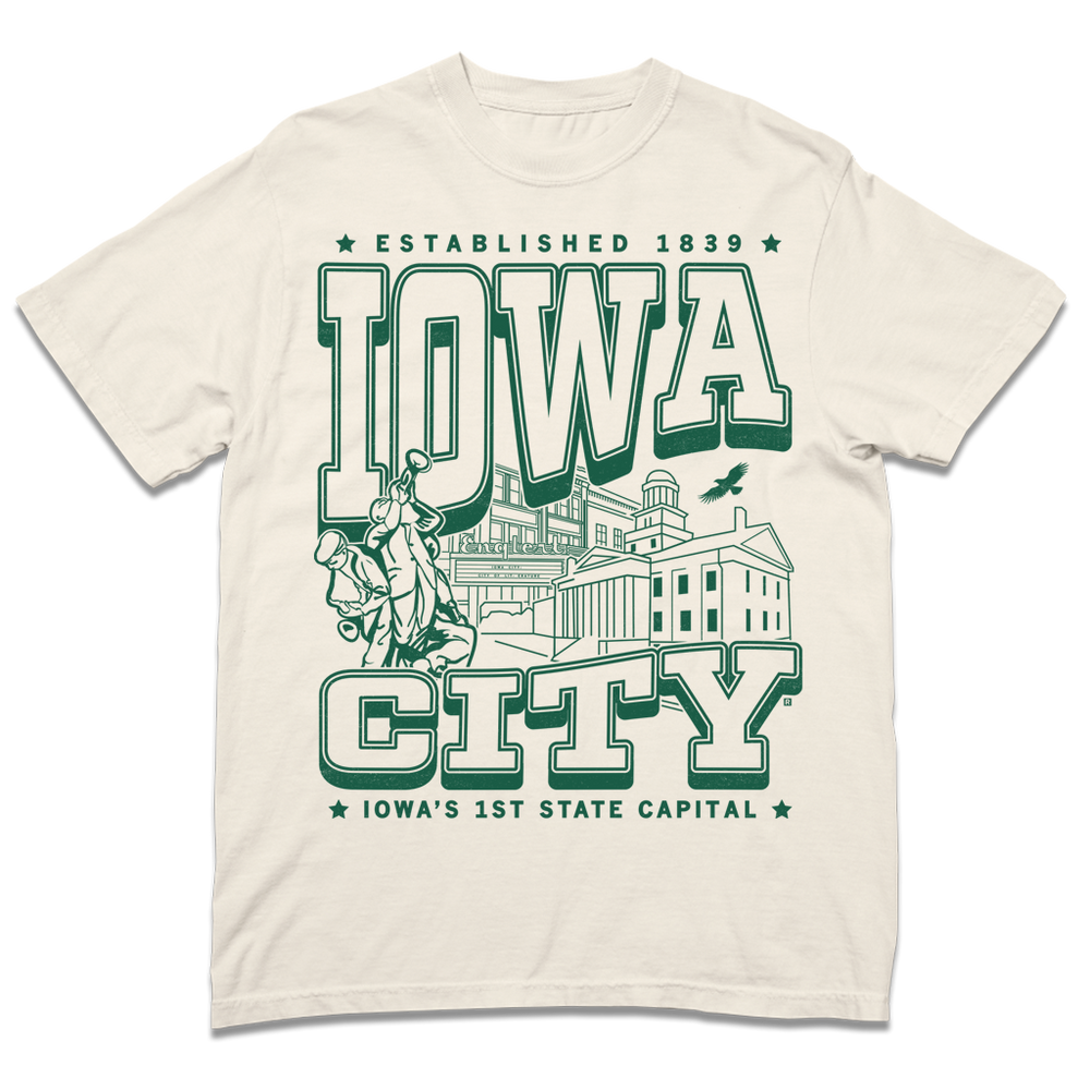 A Comfort Colors heavyweight ivory t-shirt with kelly green ink that says, "Iowa City: Established 1839. Iowa's first state Capital" with and illustrated Iowa City staples in the center, including the Englert Theater and the old Capitol Building.