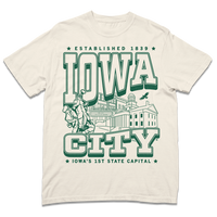 A Comfort Colors heavyweight ivory t-shirt with kelly green ink that says, "Iowa City: Established 1839. Iowa's first state Capital" with and illustrated Iowa City staples in the center, including the Englert Theater and the old Capitol Building.