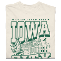A folded heavyweight cream t-shirt with kelly green ink that says, "Iowa City: Established 1839. Iowa's first state Capital" with and illustrated Iowa City staples in the center, including the Englert Theater and the old Capitol Building.