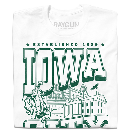 A folded white t-shirt with kelly green ink that says, "Iowa City: Established 1839. Iowa's first state Capital" with and illustrated Iowa City staples in the center, including the Englert Theater and the old Capitol Building.