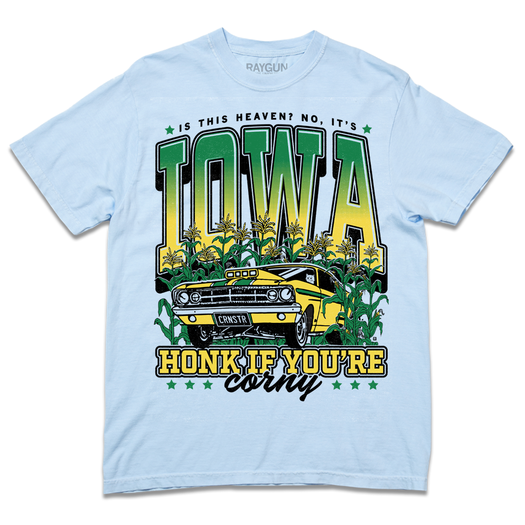 A Comfort Colors hydrangea t-shirt with green & gold ink that says, "Is this heaven? No, It's Iowa. Honk if you're corny" with a graphic of an old muscle car driving out of corn fields with a cat behind the steering wheel.